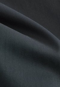 Gros plan d'un tissu noir tissé serré avec une texture côtelée diagonale et des plis doux créant des ombres.