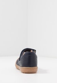 Navy kožená bota s texturačními hnědými gumovými podrážkami, zdobená dekorativními perforacemi a jemným páskem vzadu.