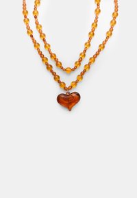 Perlenkette mit bernsteinfarbenen, runden Perlen, verbunden mit einem durchscheinenden Herzanhänger. Strukturierte Oberfläche und geschichtetes Design.