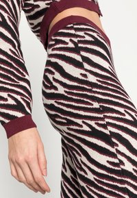 Conjunto de roupa de malha com riscas de zebra em preto e branco, realçado com bordô nas mangas e na cintura, exibindo um design justo.