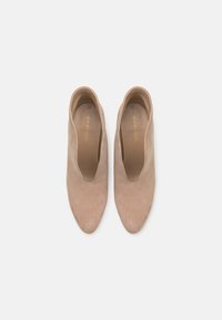 Bottes chevilles en daim nude avec un bout pointu et un design en V. Texture lisse, sans éléments métalliques apparents, style minimaliste.