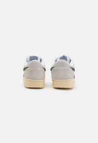 Grå og grønn joggesko med glatt lær overdel, hvit mesh-tunge, polstret krage og beige gummisåle. Enkel, lav toppdesign.