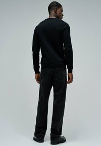 Camisa negra de manga larga con escote redondo, combinada con pantalones de pana negros. Textura suave y ajuste estándar con dos bolsillos traseros.