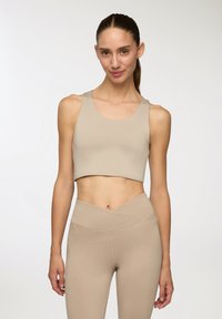 Top corto atletico beige con scollatura rotonda e spalline larghe, abbinato a leggings beige a vita alta con un cinturino asimmetrico.
