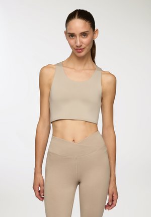 Top corto atletico beige con scollatura rotonda e spalline larghe, abbinato a leggings beige a vita alta con un cinturino asimmetrico.