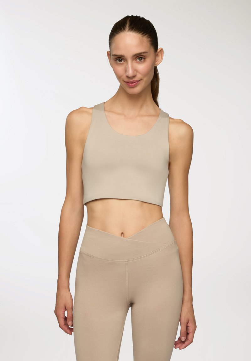 Top corto atletico beige con scollatura rotonda e spalline larghe, abbinato a leggings beige a vita alta con un cinturino asimmetrico.