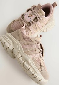 Baskets rose clair en mesh et en daim, dotées d'un patch de personnage bien visible, d'une semelle texturée et de lacets élastiques pour un enfilage facile.