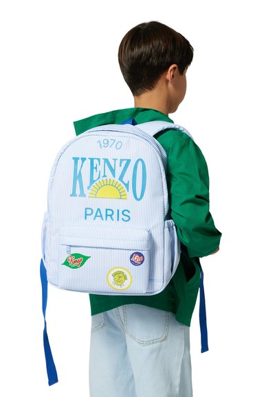Zaino a strisce blu e bianche con la scritta "KENZO PARIS", grafica del sole e toppe colorate. Presenta spallacci imbottiti e una tasca frontale.