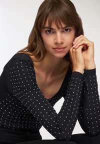 Maglietta nera a maniche lunghe con scollatura a barco, coperta da piccole borchie argentate, con vestibilità slim e tessuto liscio e elastico.