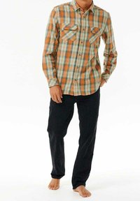 Camicia di flanella a quadri arancione e teal con due tasche sul petto, collo con bottoni e maniche lunghe; abbinata a pantaloni neri.