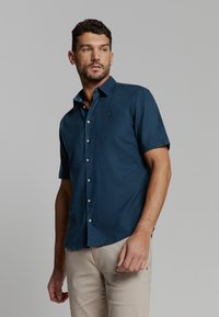 Korte mouwen overhemd met knoopsluiting in donkerblauw, gemaakt van lichtgewicht stof. Voorzien van een kraag, een voorste placket en een subtiele logo op de borst.