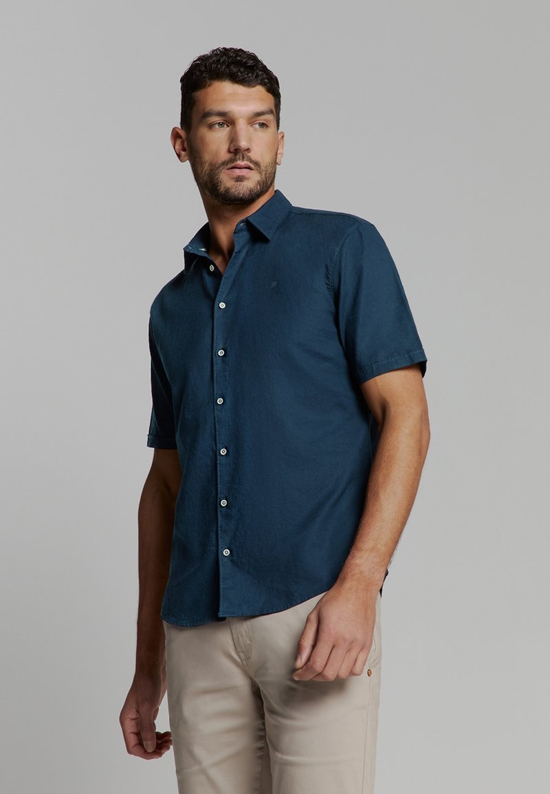 Korte mouwen overhemd met knoopsluiting in donkerblauw, gemaakt van lichtgewicht stof. Voorzien van een kraag, een voorste placket en een subtiele logo op de borst.