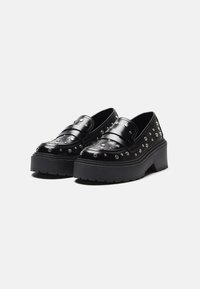 Chaussures à plateforme noires en cuir avec des détails cloutés et une semelle épaisse et texturée. Présente un design à enfiler et des bandes larges sur le devant.