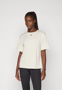 Lichtbeige t-shirt met korte mouwen gemaakt van gladde stof. Heeft een zwart Puma-logo gecentreerd op de borst. Eenvoudig, relaxed fit ontwerp.
