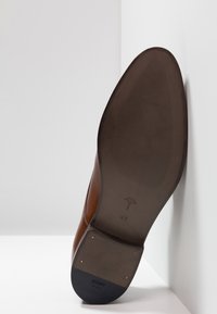 Zapato de cuero marrón con puntera puntiaguda, que presenta una suela de goma, textura acanalada y detalles metálicos en la base. Talla 41.
