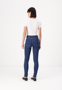 Chudé džiny v tmavomodrom denim, s vysokým pásom, dvoma zadnými vreckami a hladkou textúrou, skombinované s priliehavým bielym topom.