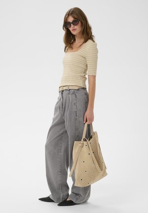 Mujer con top beige de rayas, jeans anchos grises, zapatos negros puntiagudos, gafas de sol, llevando un bolso grande beige con ojales.