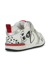 Sneakers bianche con un design a macchie nere, un accento argentato e il viso di un cane disegnato. Cinghia in velcro per indossarle facilmente. Tab sul tallone rosso.