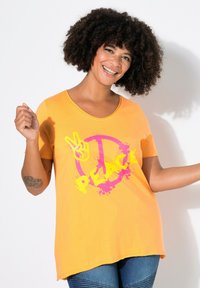 T-shirt en coton orange à manches courtes, arborant un grand texte "PEACE" en jaune et un symbole de paix en rose avec un design éclaboussé.