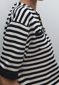 Randig stickad topp med marinblå, vit och guldfärgade ränder, korta ärmar, rund halsringning och tre guldknappar framtill.