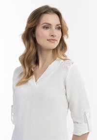 Hvid linned bluse med V-hals, trekvartærmer og blondedetaljer på skuldrene, med en tekstureret stoffinish.