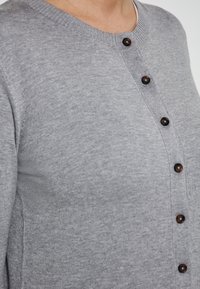 Grauer Cardigan mit rundem Ausschnitt, durchgehender Knopfleiste und dunklen Knöpfen. Glatte, gestrickte Textur mit gerippten Bündchen und Saum.