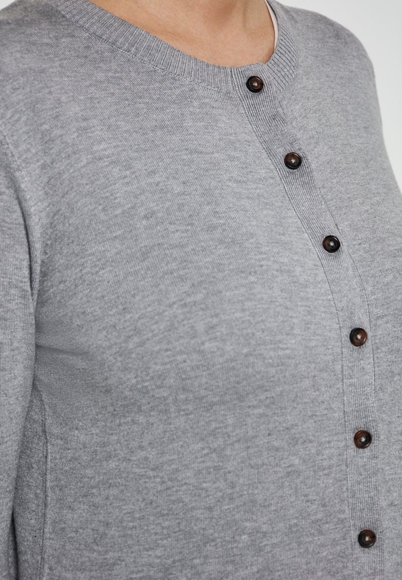 Grauer Cardigan mit rundem Ausschnitt, durchgehender Knopfleiste und dunklen Knöpfen. Glatte, gestrickte Textur mit gerippten Bündchen und Saum.