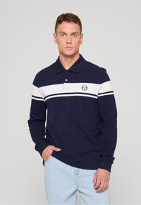 Tmavomodrá polokošeľa s dlhými rukávmi, bielymi vodorovnými pruhmi a logom, s golierom a rovnými lemami. Neformálny strih.