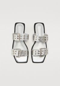 Sandales en métal argenté avec un bout carré, dotées de deux larges brides ornées de boucles et de rivets décoratifs, et d'une semelle noire.