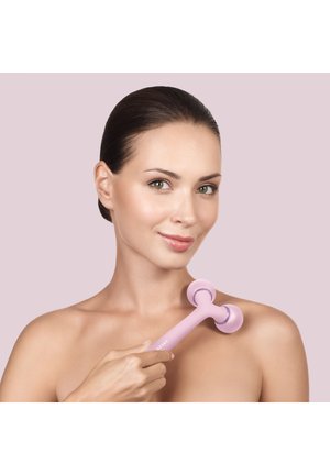 Kvinde bruger en håndholdt lyserød ansigtsmassage-rulle på sin skulder mod en lys mauve baggrund.