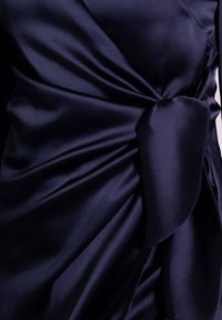 Robe en satin bleu marine avec du tissu drapé et un grand nœud latéral, présentant une texture lisse et des plis élégants sur l'ensemble du tissu.