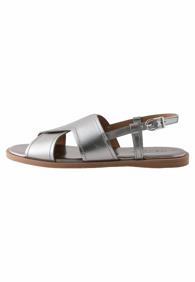 Sandalo in pelle argentata con design open-toe, fasce incrociate, fibbia regolabile alla caviglia e suola piatta. Texture liscia, stile minimalista.