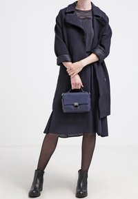 Námořnický kabát s texturovanou tkaninou, oversize střih a ohrnuté rukávy. Nositý přes odpovídající šaty, doplněný malou modrou kabelkou a kotníkovými botami.