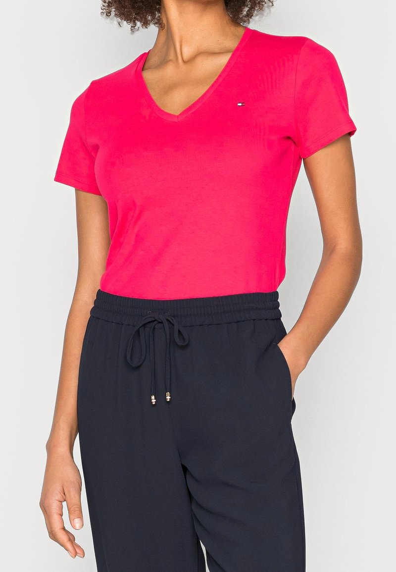 Lyserød V-neck t-shirt lavet af blødt bomuld, med korte ærmer og et lille logo på brystet, kombineret med navy blå bukser med snoretræk.