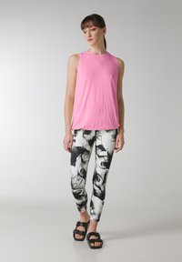 Lyserød ærmeløs top med en afslappet pasform, parret med leggings i sort og hvid med abstrakte blomstermønstre og sorte sandaler.