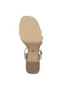 Sandal con cinturino alla caviglia e suola beige, texture rigata e logo in rilievo. La parte superiore presenta dettagli metallici e elementi decorativi.
