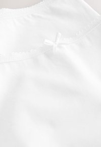 Tissu blanc à texture lisse, orné d'une délicate bordure en dentelle et d'un petit nœud blanc au creux de la nuque à l'arrière.