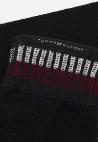 Svart strikkegenser med et flerfarget stripemønster i rød, hvit og marineblå nær kragen. Har en svart etikett med "TOMMY HILFIGER."