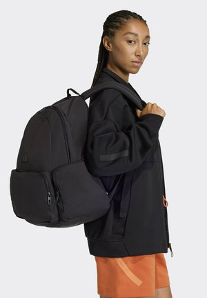 Zaino nero in tessuto resistente, con compartimento principale con cerniera, tasca frontale e spallacci regolabili. Dettaglio arancione a contrasto.