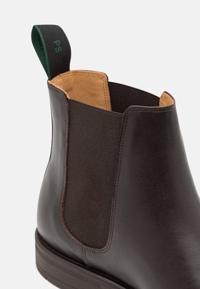 Mørkebrun skinn Chelsea-støvel med elastisk sidepanel, lys lærinteriør og svart trekksløyfe med grønn skrift.