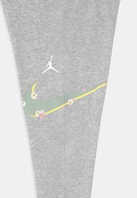 Szare spodnie sportowe z zielonym i żółtym wzorem w kształcie smoka, ozdobione małymi kwiatkami, oraz białym logo Jordana na lewym nogawce.