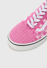 Roze geweven sneakers hebben een textuurstof bovenkant, witte veters en een wit logo. De zool is van rubber met een zwarte accentrand.