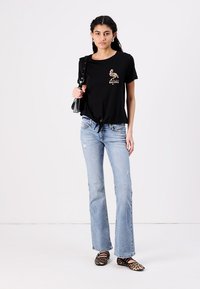 Black cropped t-shirt with a flamingo graphic, light blue flared jeans, and leopard print flats. Accessories include a black handbag.