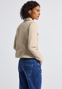 Veste en denim beige au toucher doux, coupe ajustée, et poches avant. Associée à un jean bleu taille haute au design classique.