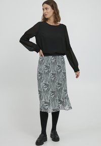 Sorte bluse med lange ærmer og samlede manchetter, parret med en mønstret midikjole med en lys baggrund og sorte bladlignende designs.