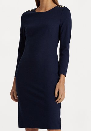 Robe longue à manches longues bleu marine moulante avec un col rond et des boutons dorés sur les deux épaules, portée par une personne debout.