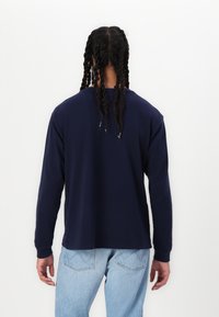 Navy long-sleeve shirt with a round neckline, soft texture, and relaxed fit. Paired with light blue denim jeans, showcasing a casual style.