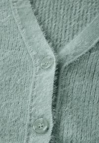 Ljusgrön cardigan gjord av mjukt, texturerat tyg. Har en V-ringning, fransade kanter och klara, runda knappar.