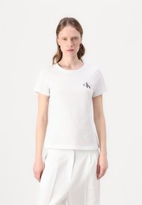 Biela bavlnená tričko s krátkym rukávom, okrúhlym výstrihom a malým čiernym logom "CK Jeans" na ľavej hrudi. Hladká textúra.