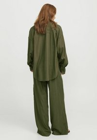 Chemise olive verte surdimensionnée avec des manches longues et un ourlet arrondi, associée à un pantalon ample assorti. Tissu doux et texturé.